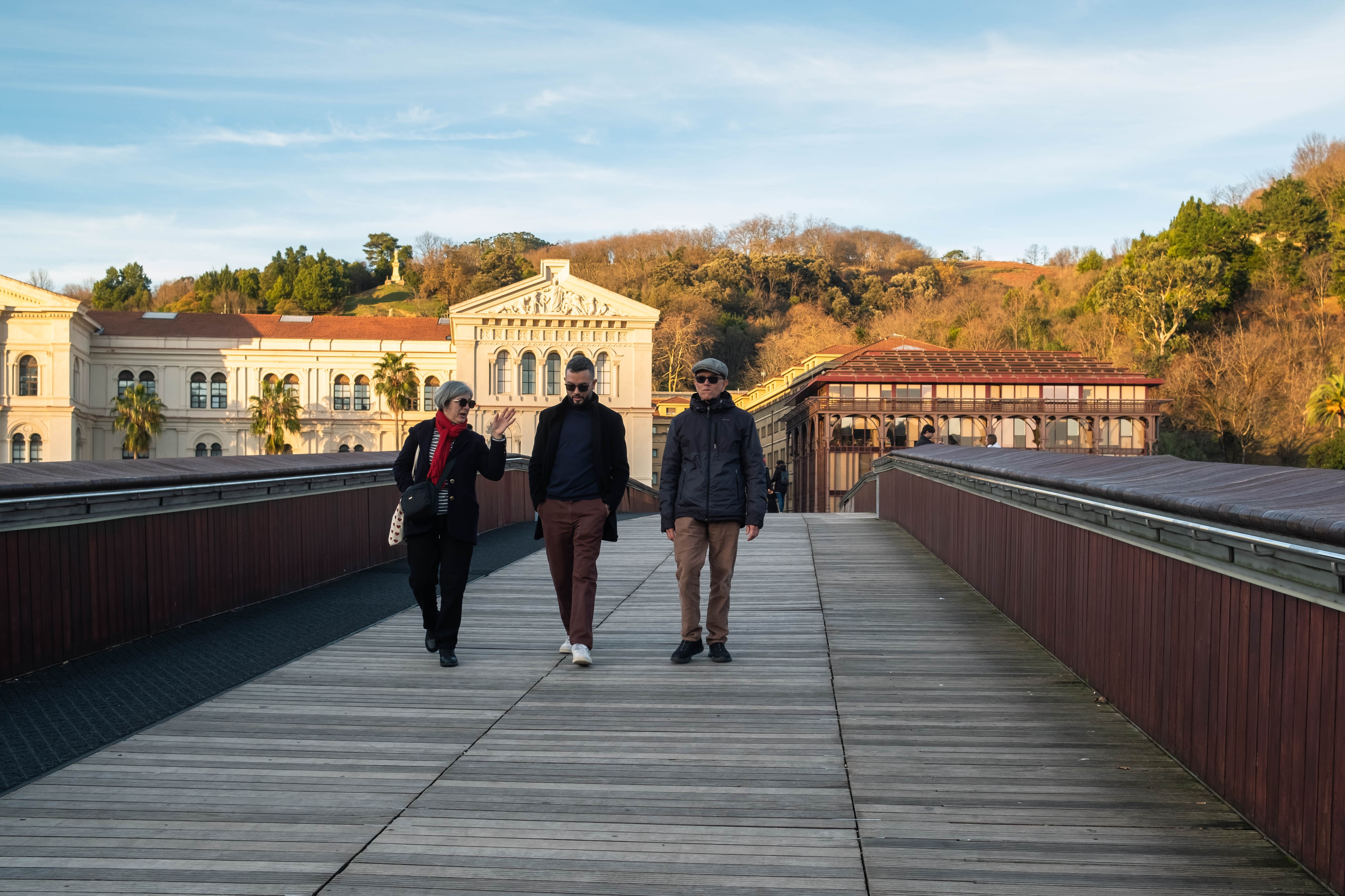 Tres personas caminan por la pasarela Pedro Arrupe, frente a la Universidad de Deusto. Bilbao, Bizkaia.