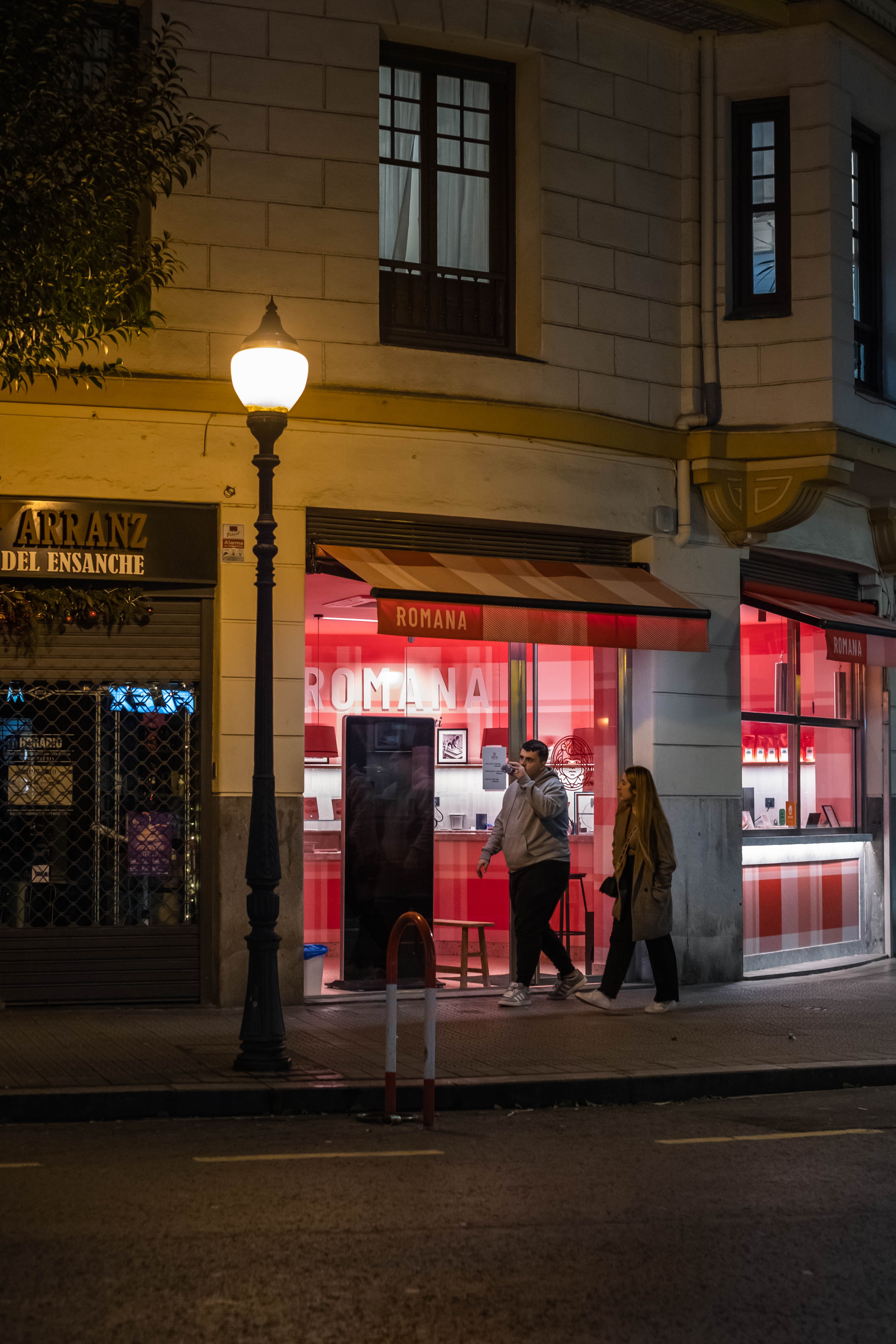 Joven pareja camina por la noche frente a un restaurante, situado en el distrito del Ensanche. Bilbao, Bizkaia.