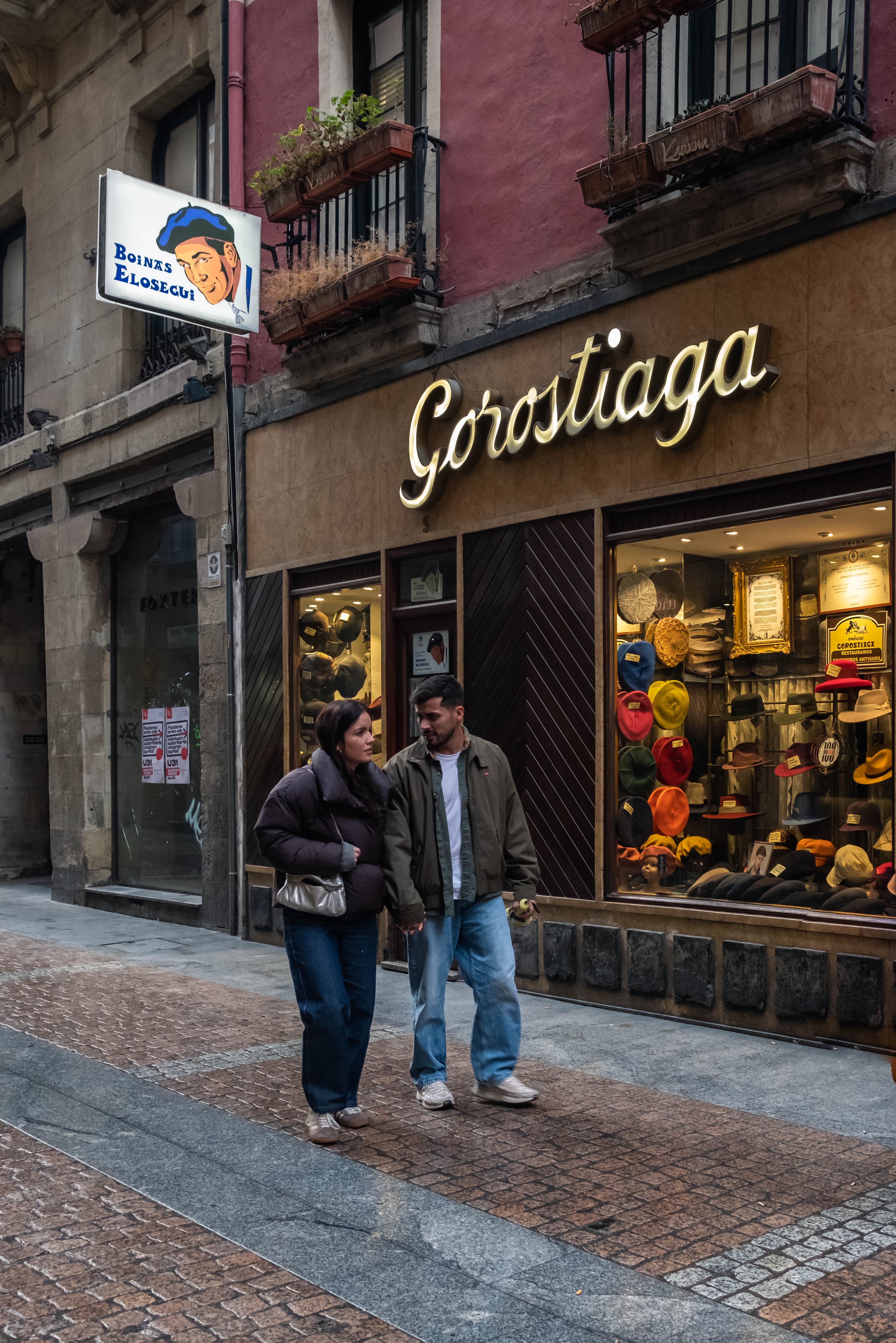 Una joven pareja camina frente a un antiguo comercio del Casco Viejo. Bilbao, Bizkaia.