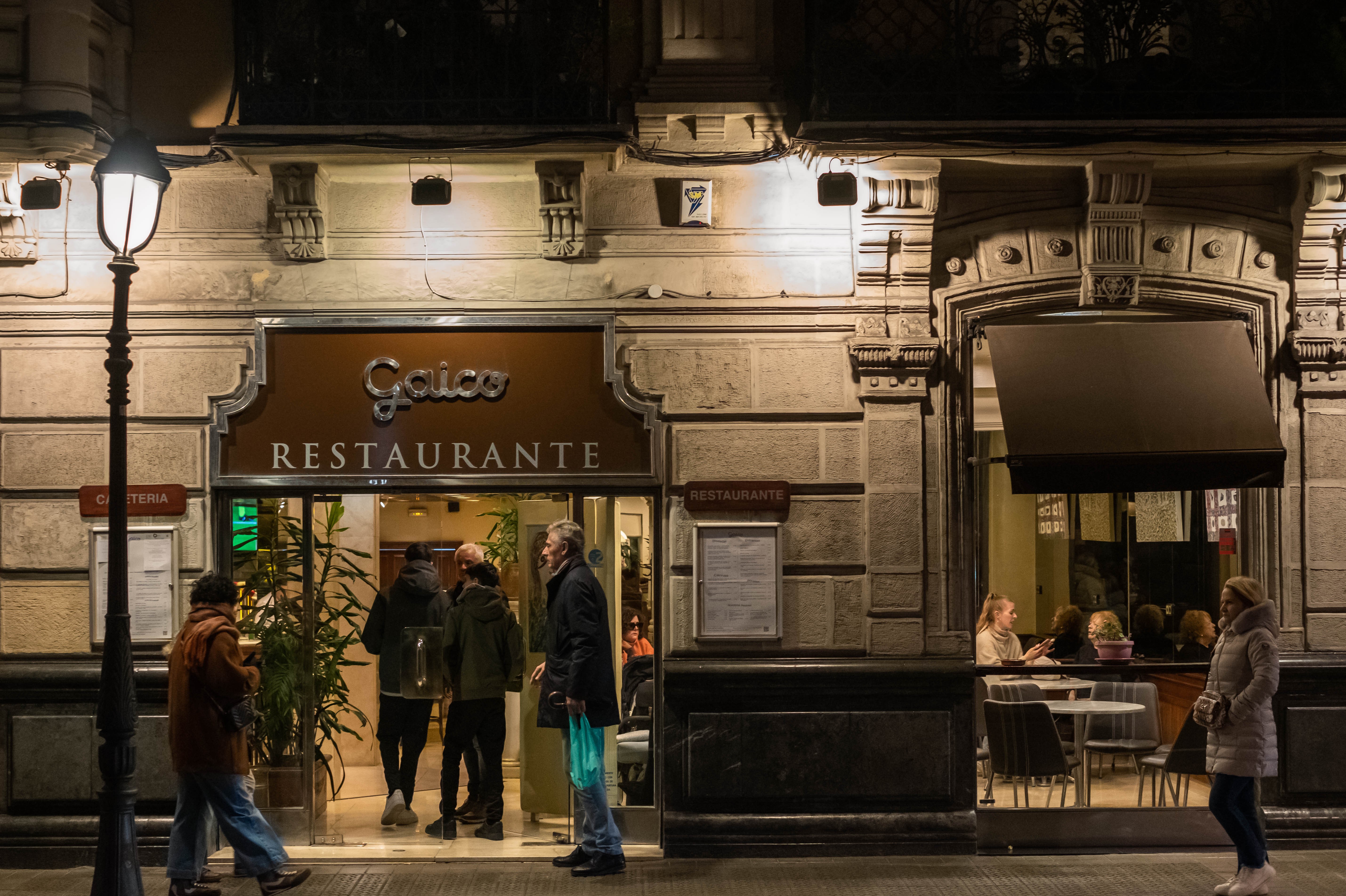 Varias personas entran de noche a un restaurante situado en el distrito del Ensanche. Bilbao, Bizkaia.