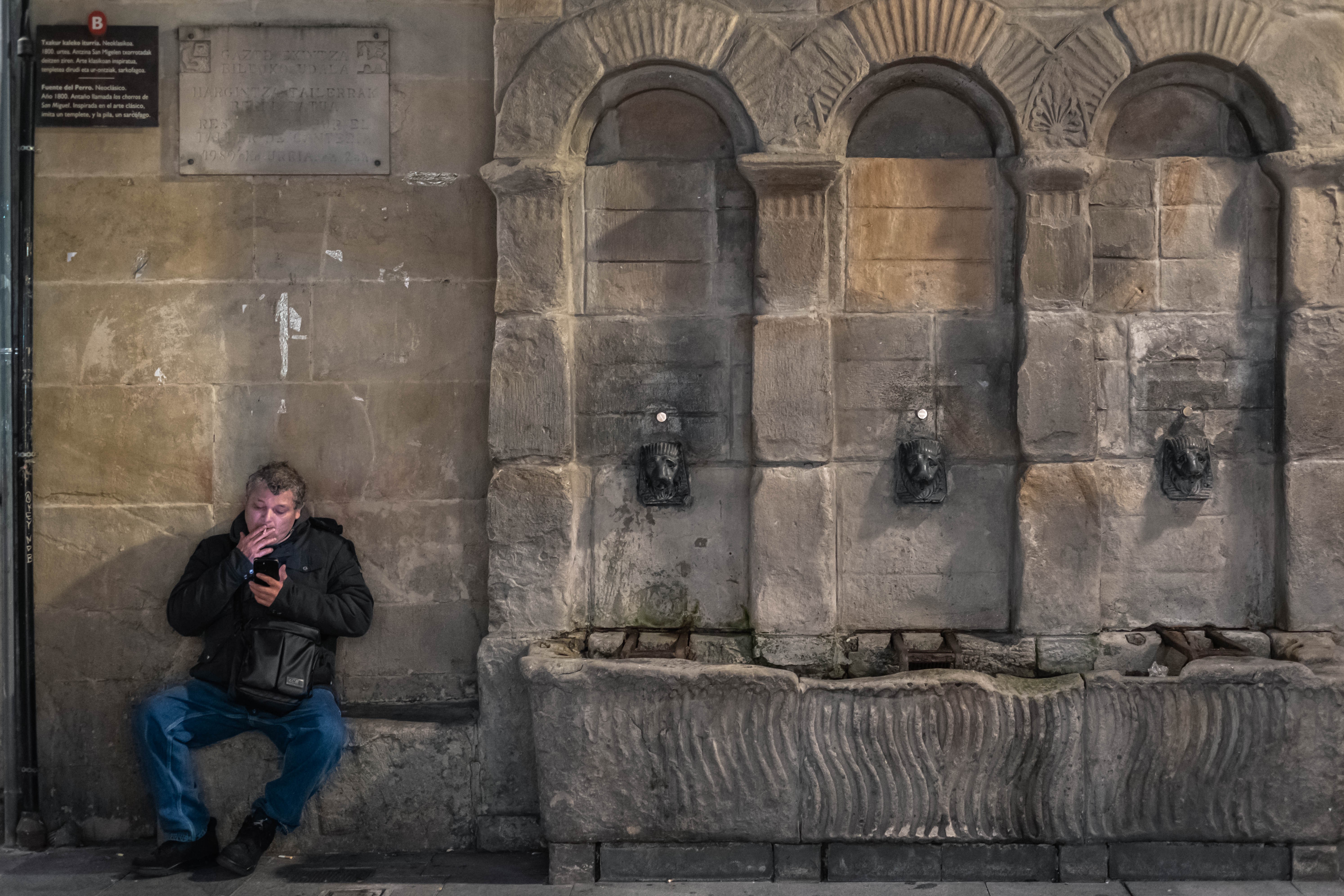 Un hombre fuma sentado junto a la fuente del Perro en el Casco Viejo. Bilbao, Bizkaia.