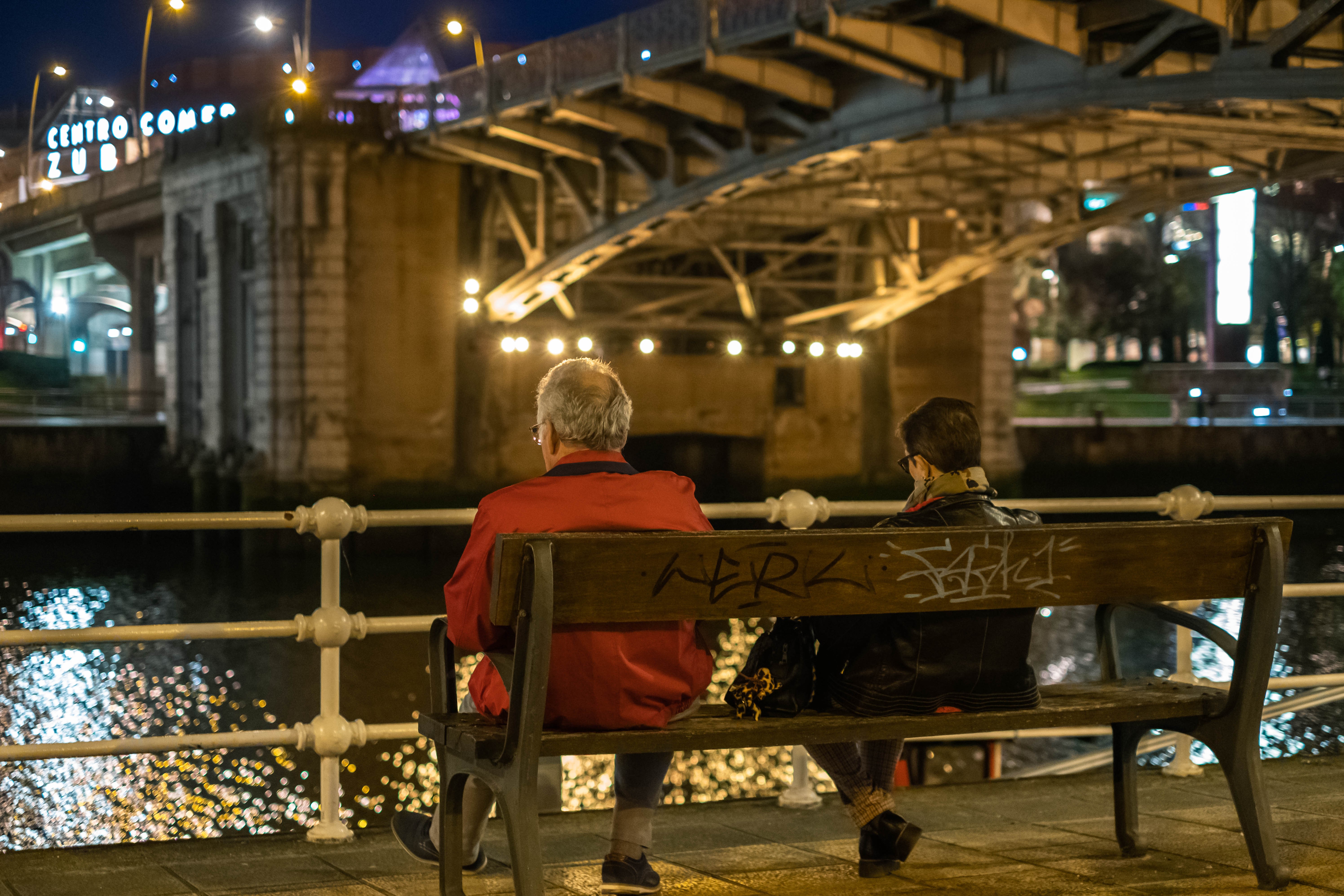 Una pareja de mediana edad descansa y contempla la ría del Nervión desde un banco bajo el Puente de Deusto. Bilbao, Bizkaia.